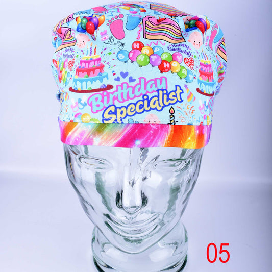 Euro-style scrub cap featuring a colorful "Birthday Specialist" cake and balloon print on a white background, shown on a mannequin head.