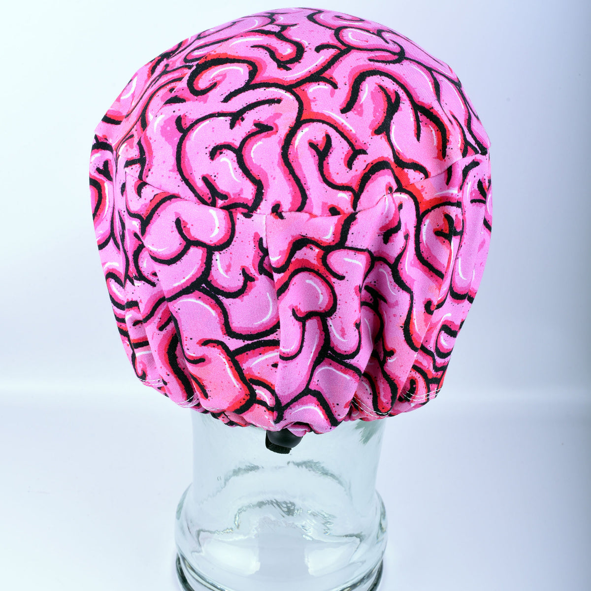 Back view of a pink brain scrub cap on a clear glass stand against a white background.