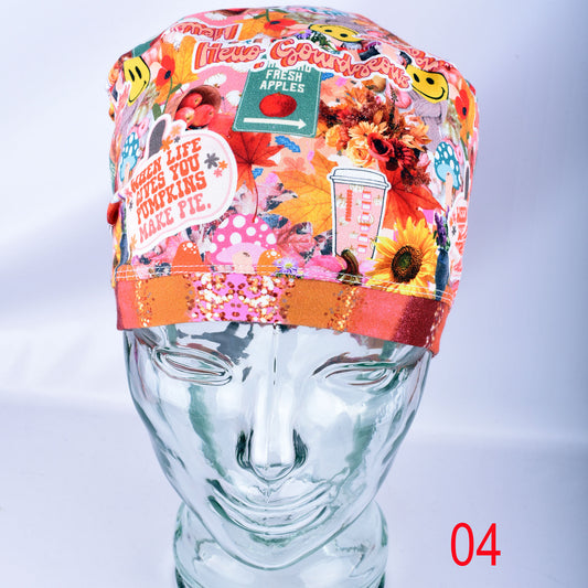 A colorful patterned fabric scrub cap displayed on a mannequin head. The cap features a busy collage print with autumn leaves, pumpkins, flowers, and text including 'WHEN LIFE GIVES YOU PUMPKINS MAKE PIE.