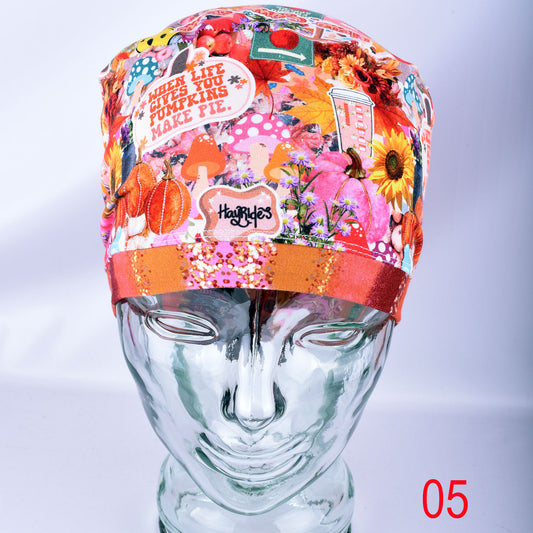 A colorful patterned fabric scrub cap displayed on a mannequin head. The cap features a busy collage print with autumn leaves, pumpkins, flowers, and text including 'WHEN LIFE GIVES YOU PUMKINS MAKE PIE.