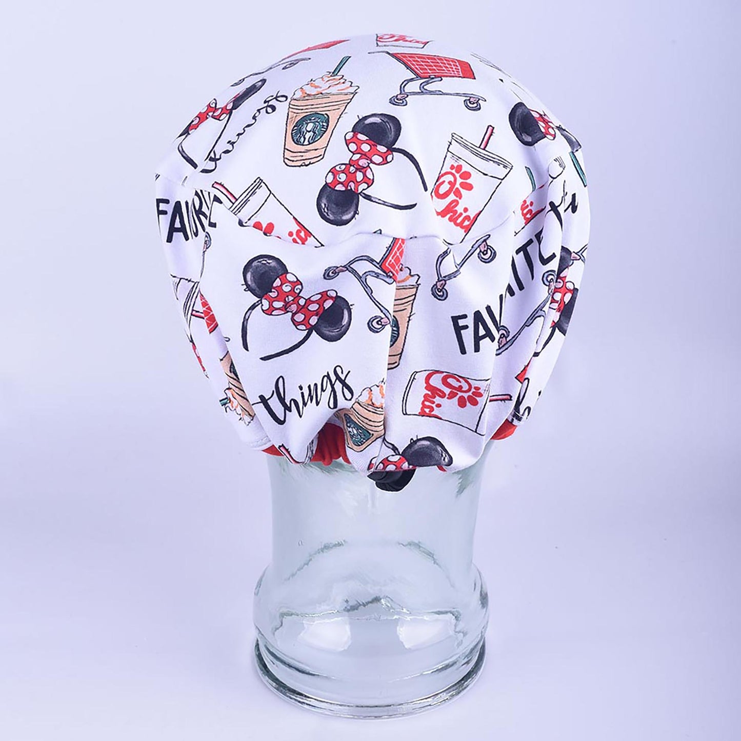 Full-coverage scrub cap featuring a playful "Favorite Things" pattern of coffee cups, shopping bags, and script lettering on a clear glass mannequin head.