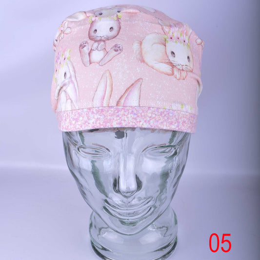 Close up of Sweet Bunnies scrub cap fabric featuring white hand-drawn bunnies and pink flowers on a soft pink background.