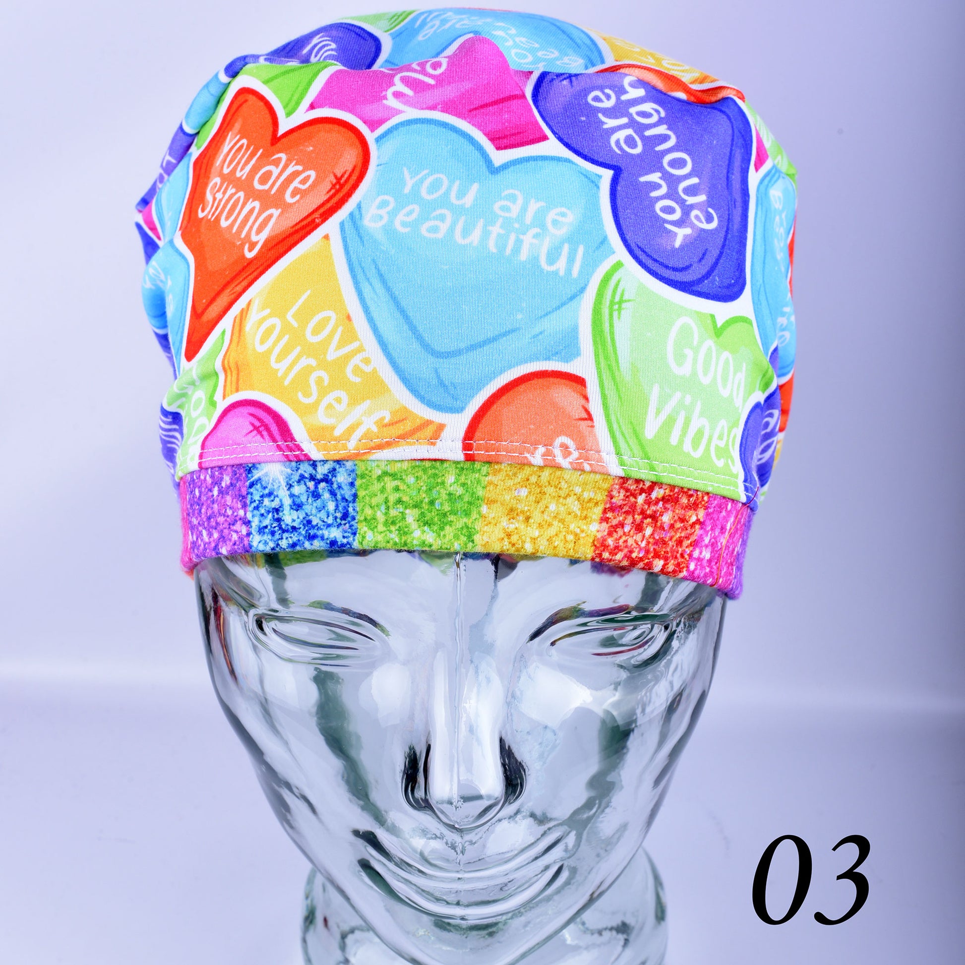 Front view of a colorful Affirmation Hearts scrub cap on a clear display head.