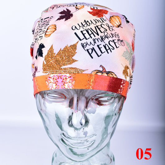 A light pink surgical cap with an autumn-themed print featuring pumpkins, leaves, and the text 'autumn LEAVES & pumpkins PLEASE', displayed on a clear glass mannequin head. The cap has a glittery orange band at the edge and a red '05' overlay in the bottom right corner.