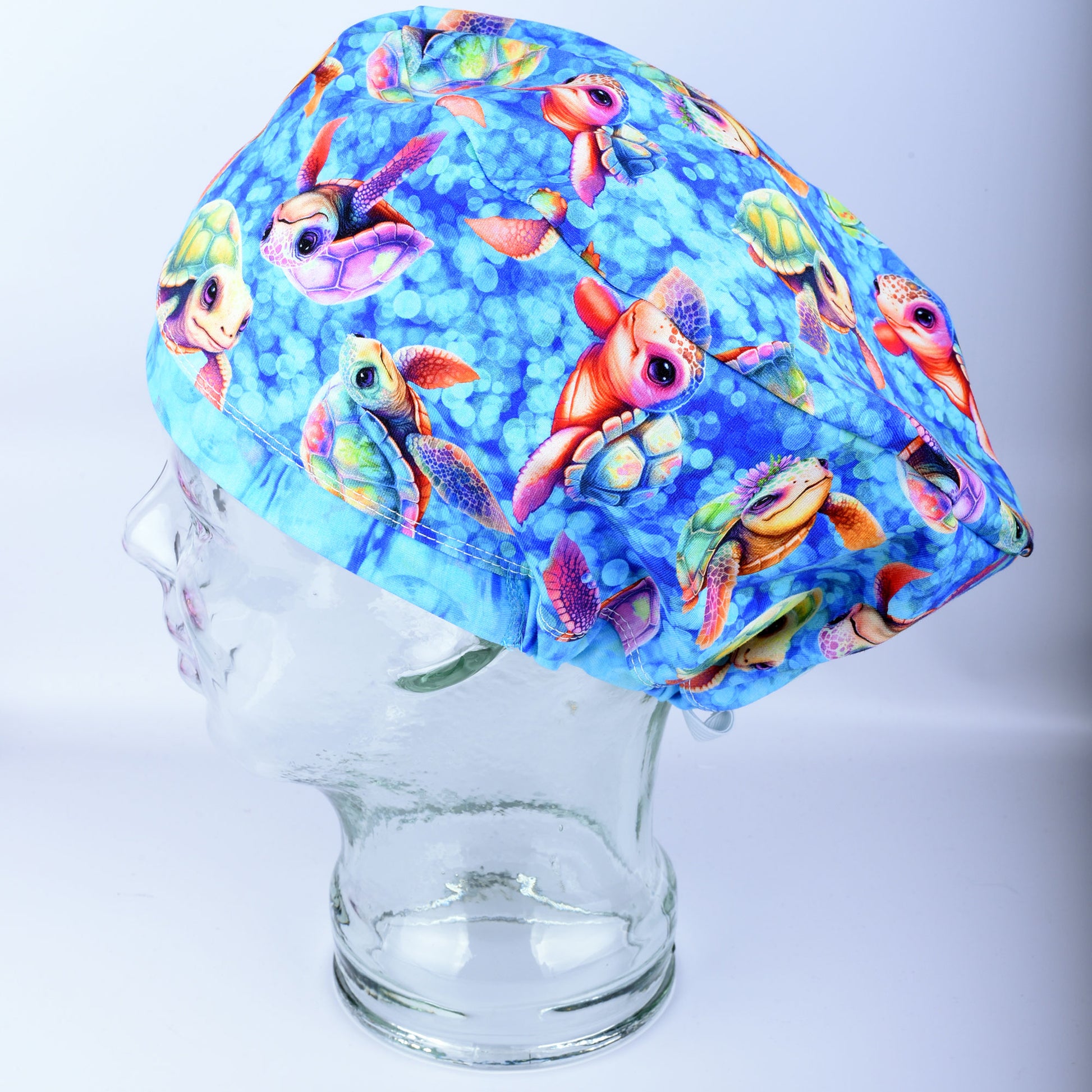 Side view of a fabric scrub cap featuring a vibrant baby sea turtle pattern on a mannequin head, showcasing the secure full coverage fit.