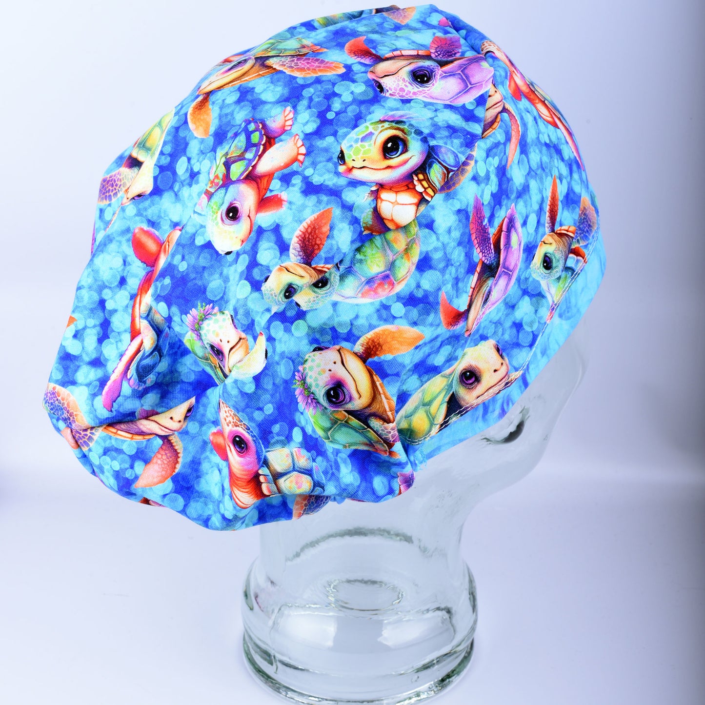 Side view of a fabric scrub cap featuring a vibrant baby sea turtle pattern on a mannequin head, showcasing the secure full coverage fit.