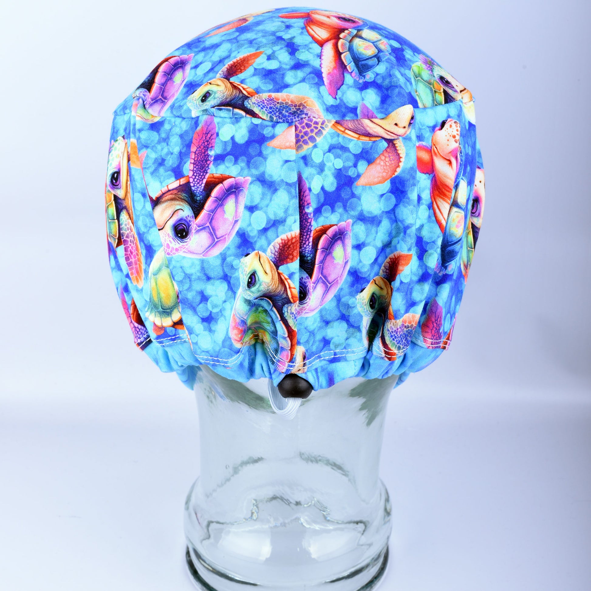 Close-up of the back of a sea turtle pattern scrub cap, highlighting the adjustable cord lock toggle and encased elastic band for a custom fit.