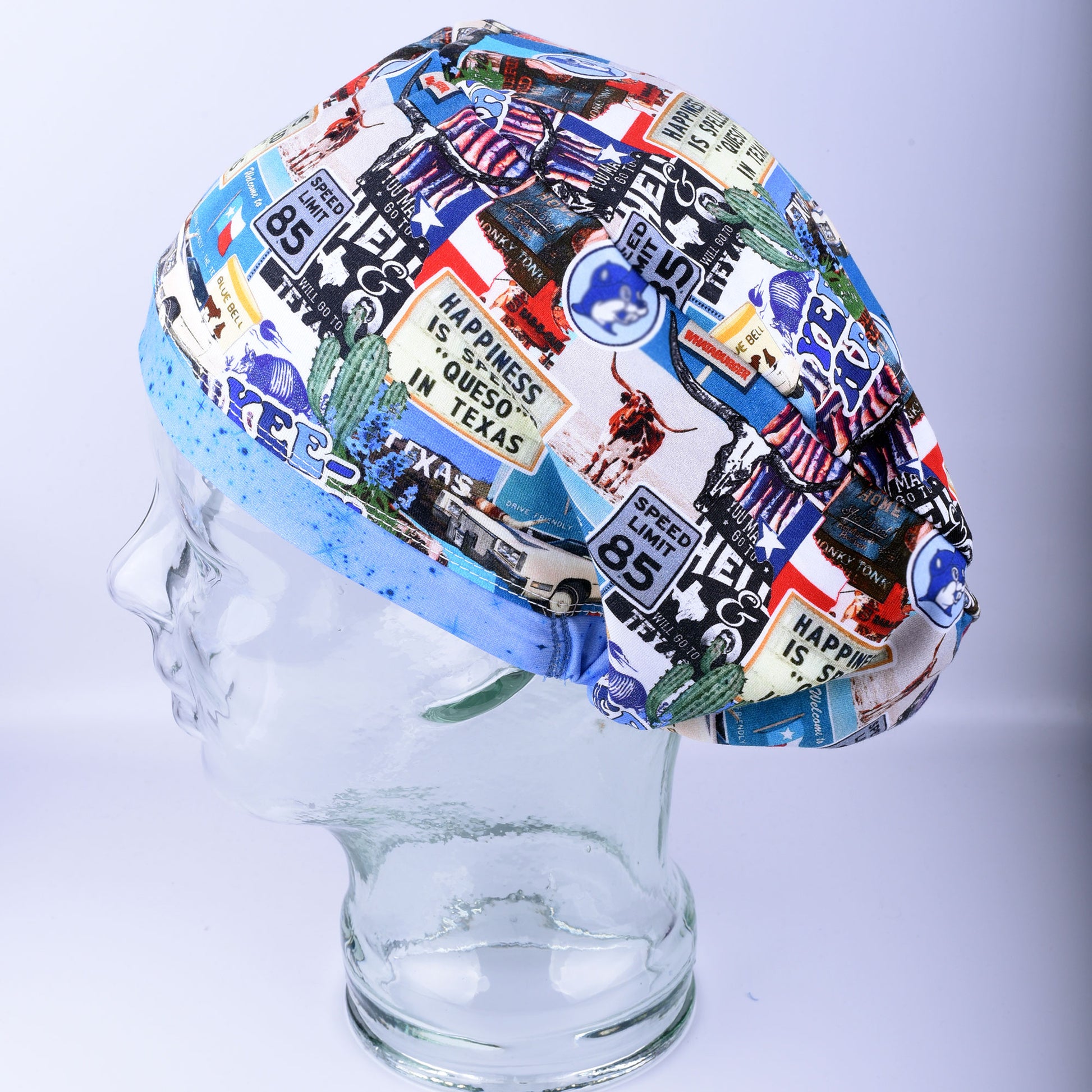 Blue Texas scrub cap on a clear display mannequin head, side view showcasing the colorful Texas-themed collage print.