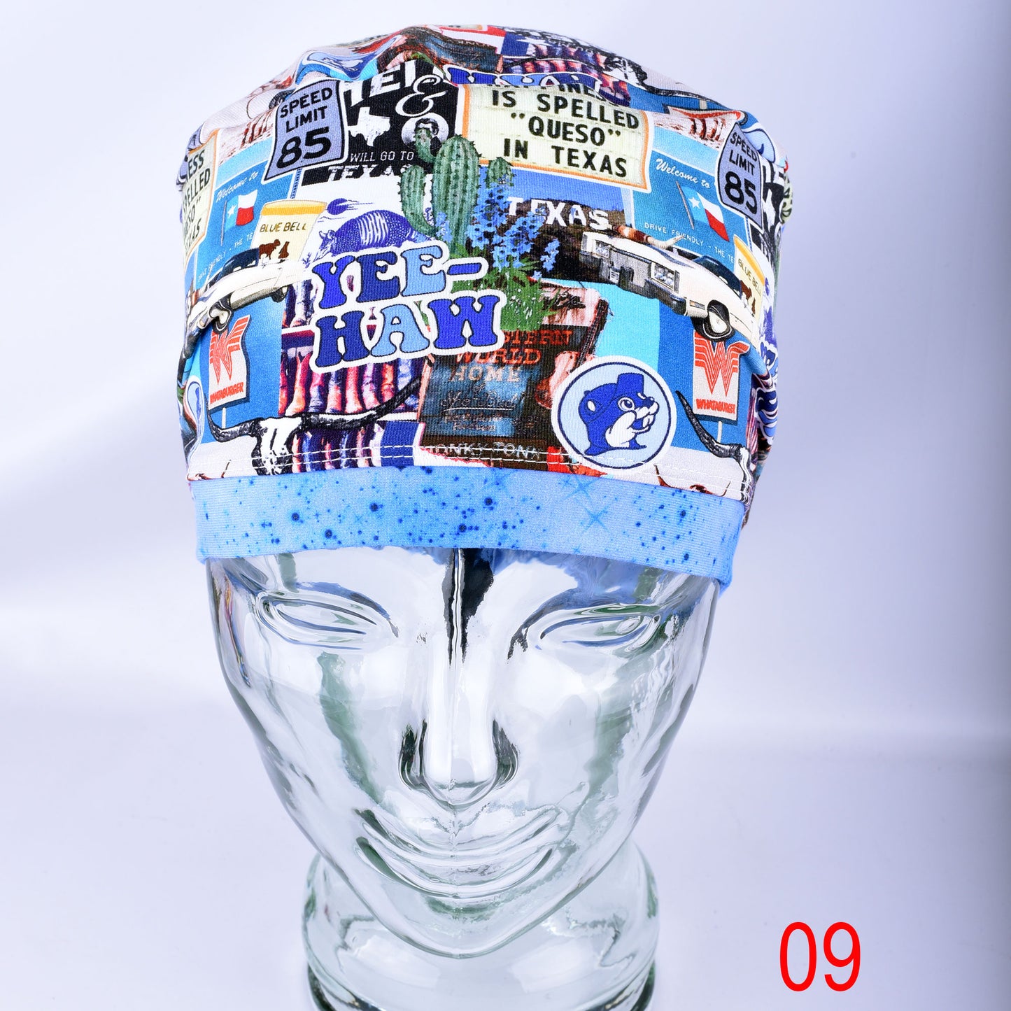 A multicolor scrub cap with a collage print featuring various vintage-style Texas travel and road-sign motifs, displayed on a clear mannequin head. The cap features a light blue elastic band at the bottom.