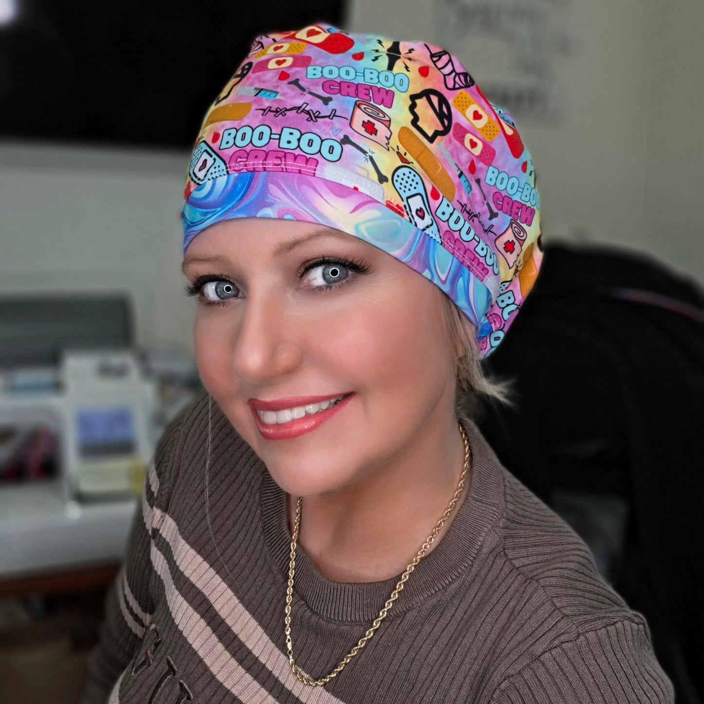 Person wearing a colorful 'Boo-Boo Chew' scrub cap in an indoor setting.