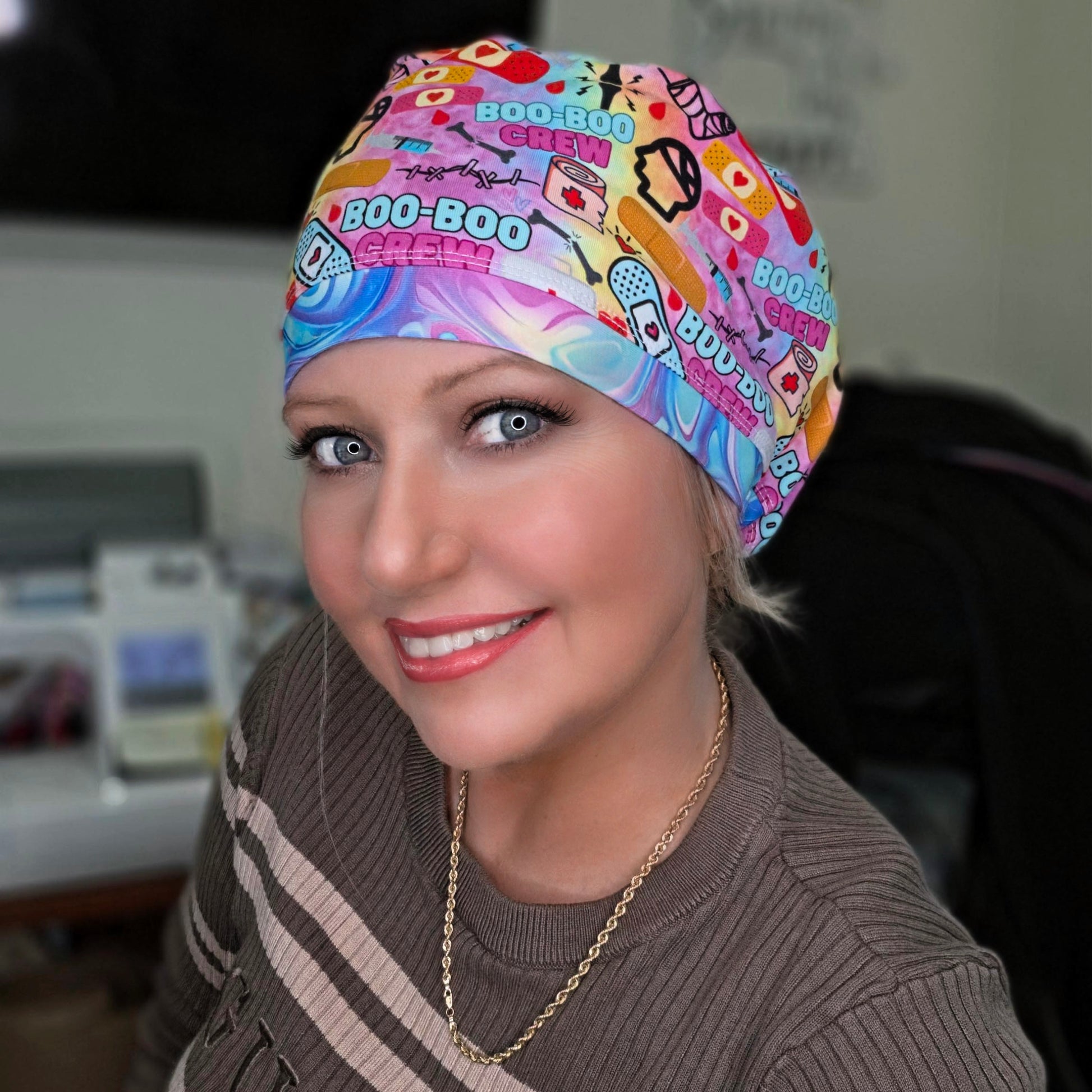 Person wearing a colorful 'Boo-Boo Chew' scrub cap in an indoor setting.