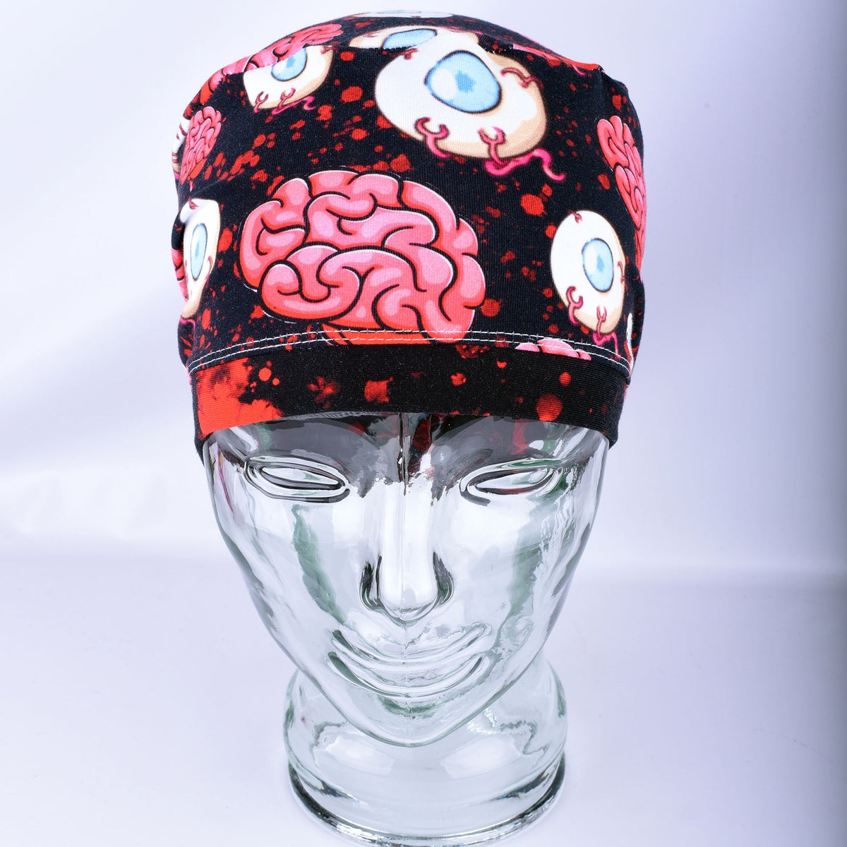Pink brain and eyeball pattern printed full-coverage medical scrub cap on a clear glass mannequin head, front angled view against a neutral gray background.