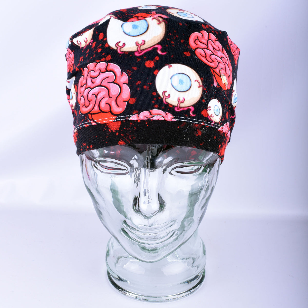 Pink brain and eyeball pattern printed full-coverage medical scrub cap on a clear glass mannequin head, front angled view against a neutral gray background.