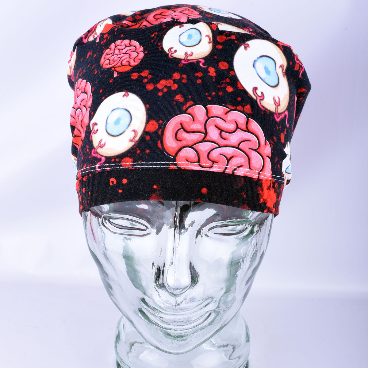 Pink brain and eyeball pattern printed full-coverage medical scrub cap on a clear glass mannequin head, front angled view against a neutral gray background.