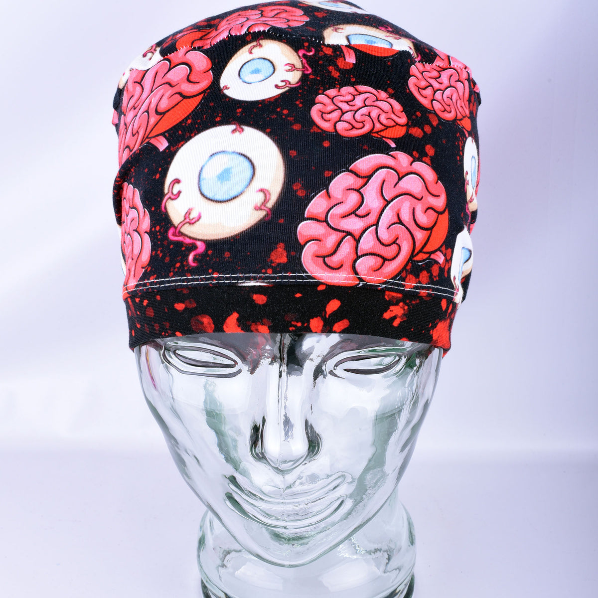 Pink brain and eyeball pattern printed full-coverage medical scrub cap on a clear glass mannequin head, front angled view against a neutral gray background.