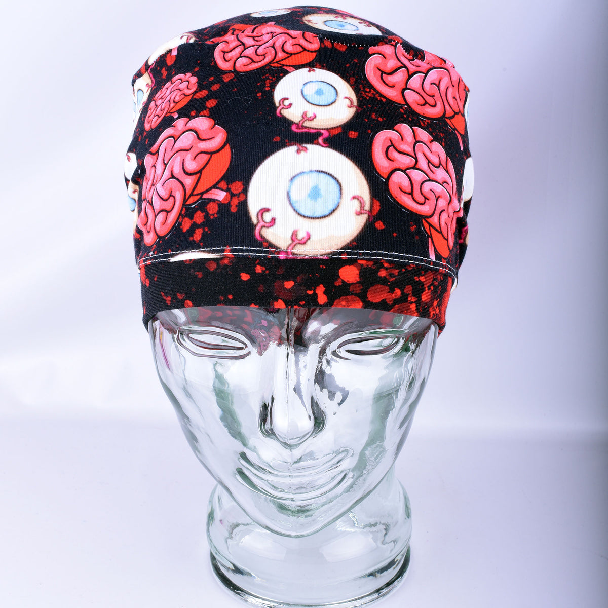 Pink brain and eyeball pattern printed full-coverage medical scrub cap on a clear glass mannequin head, front angled view against a neutral gray background.
