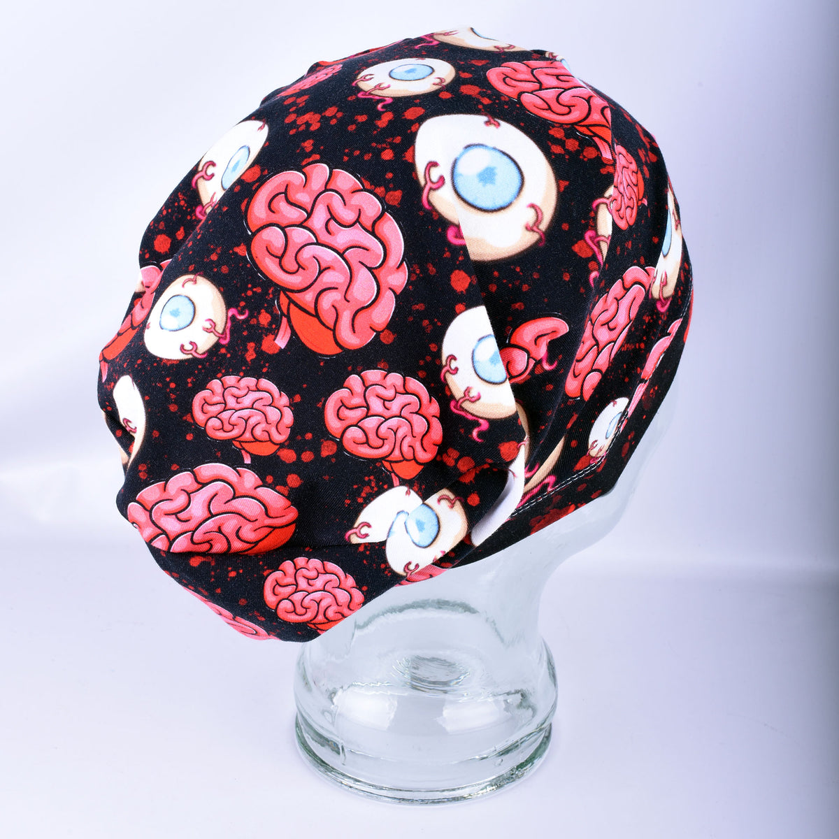 Side profile of a black full-coverage surgical scrub cap featuring a spooky brain and eyeball graphic print on a glass mannequin head.