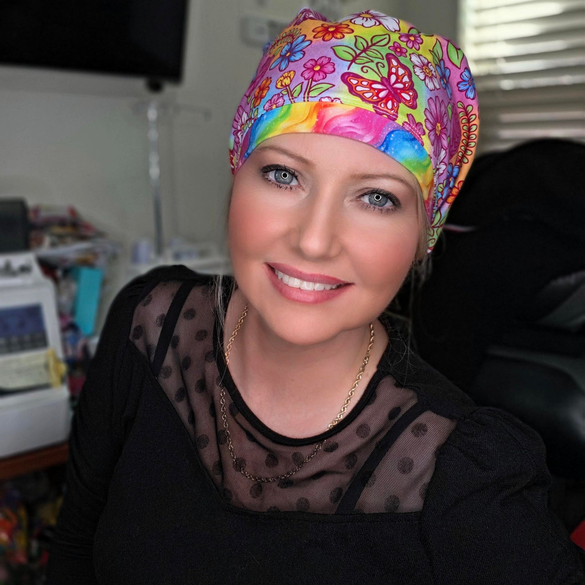 Woman wearing a Euro style scrub cap featuring a vibrant butterfly and floral print on a rainbow background with an adjustable toggle.