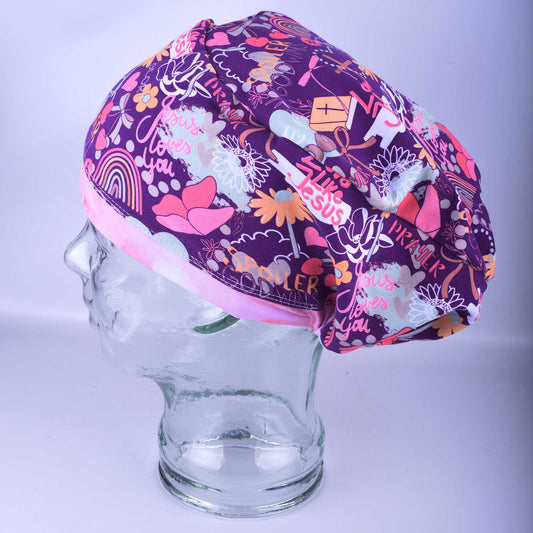 Close-up of a Euro-style scrub cap featuring a vibrant purple and pink Christian faith floral pattern with religious symbols on a white background.