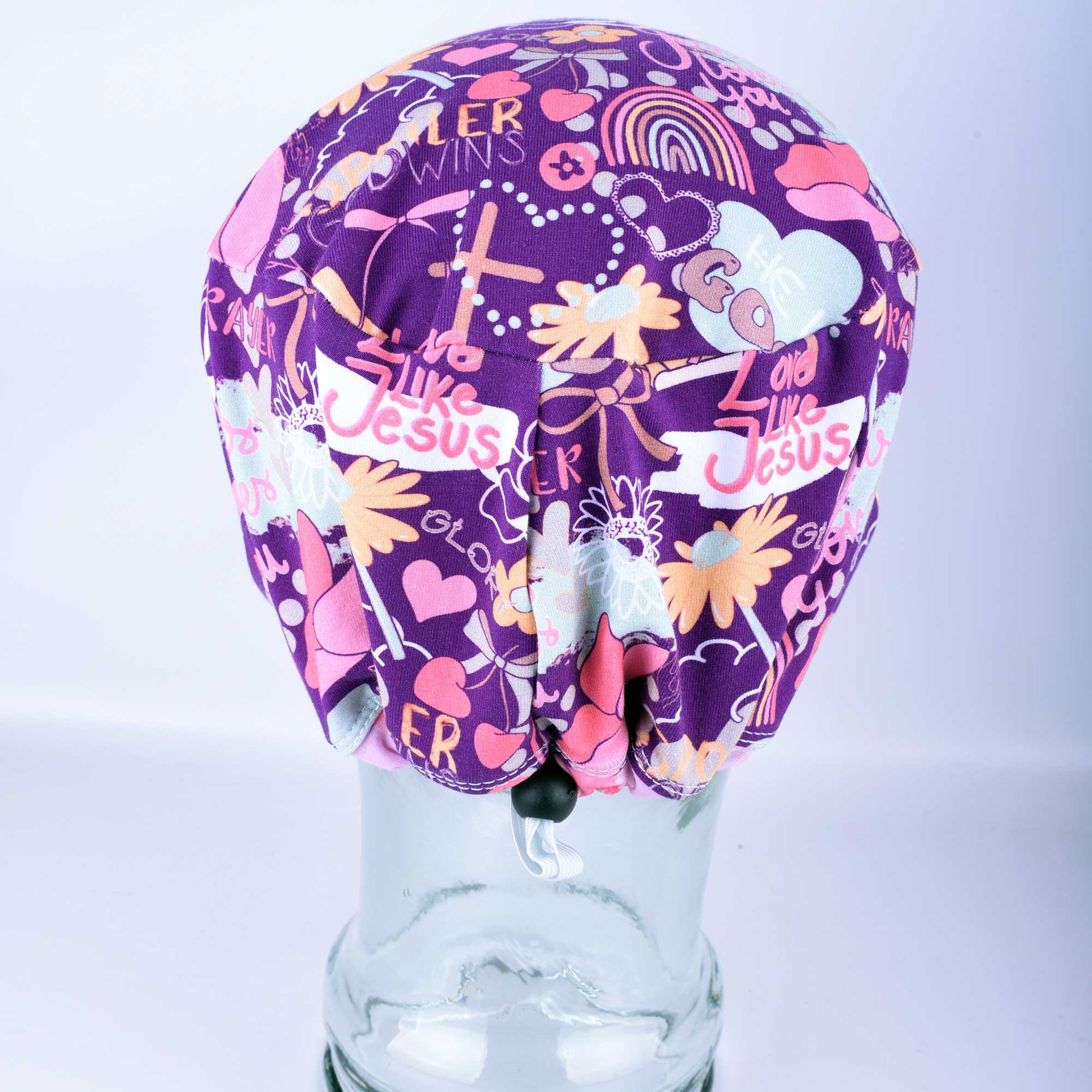 Back view of a pink and purple faith-based scrub cap showing the adjustable elastic drawstring and cord lock for a custom fit.