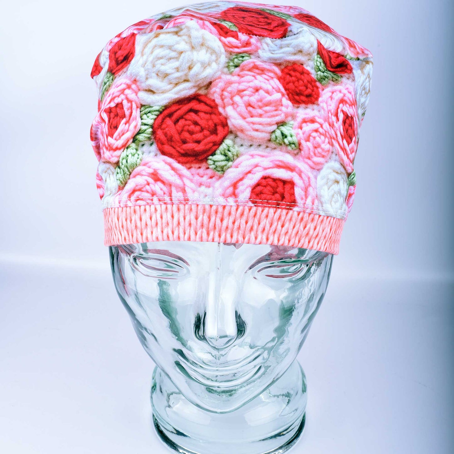 A full-coverage Euro-style scrub cap featuring a vibrant "Crochet Roses" pattern with pink and red floral motifs on a white background, displayed on a glass headform.