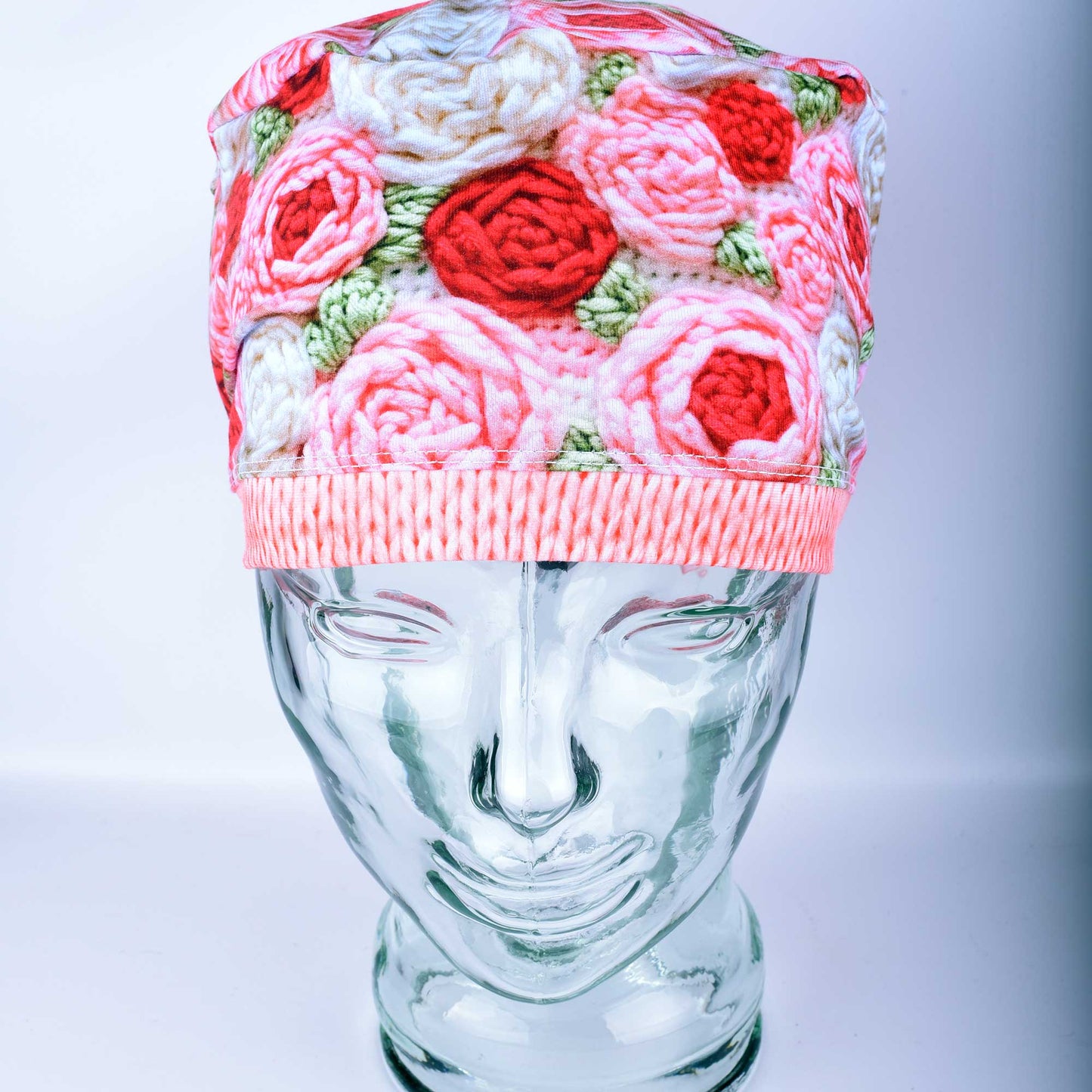 A full-coverage Euro-style scrub cap featuring a vibrant "Crochet Roses" pattern with pink and red floral motifs on a white background, displayed on a glass headform.