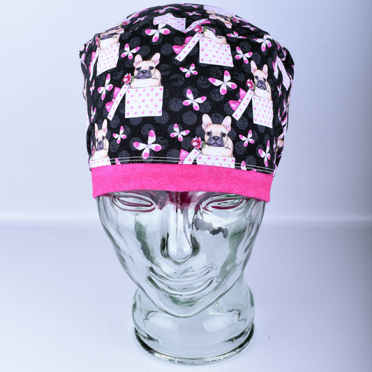 Close-up of a full-coverage scrub cap featuring a pattern of cute French Bulldog faces on a neutral background, showing the adjustable cord lock toggle and stretchy fabric texture.