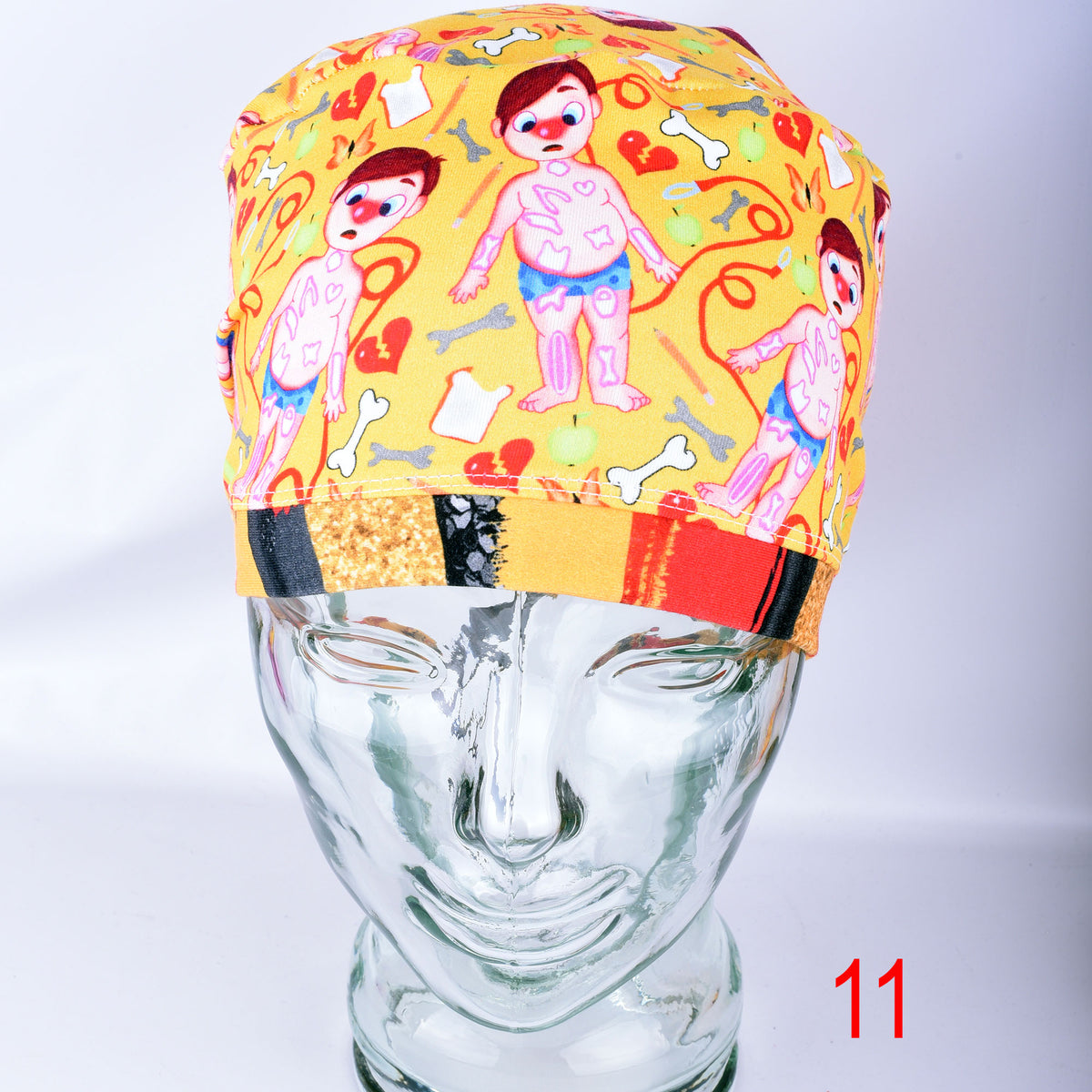 Colorful yellow scrub cap featuring cartoon medical patients and anatomical symbols on a glass mannequin head.