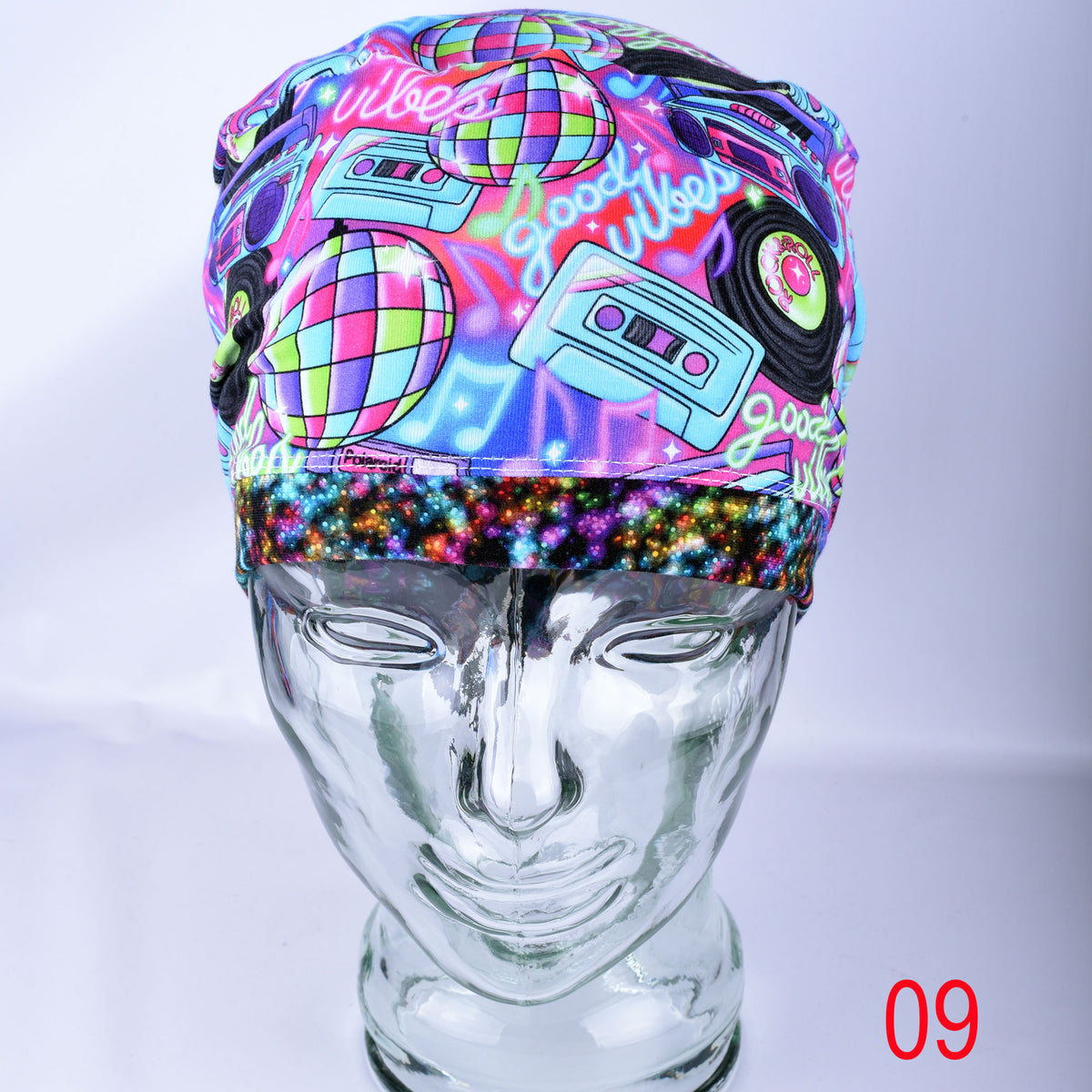 A vibrant, multicolor scrub hat with a retro 1980s/90s disco theme, featuring cassette tapes, vinyl records, and a disco ball pattern, displayed on a clear glass mannequin head.