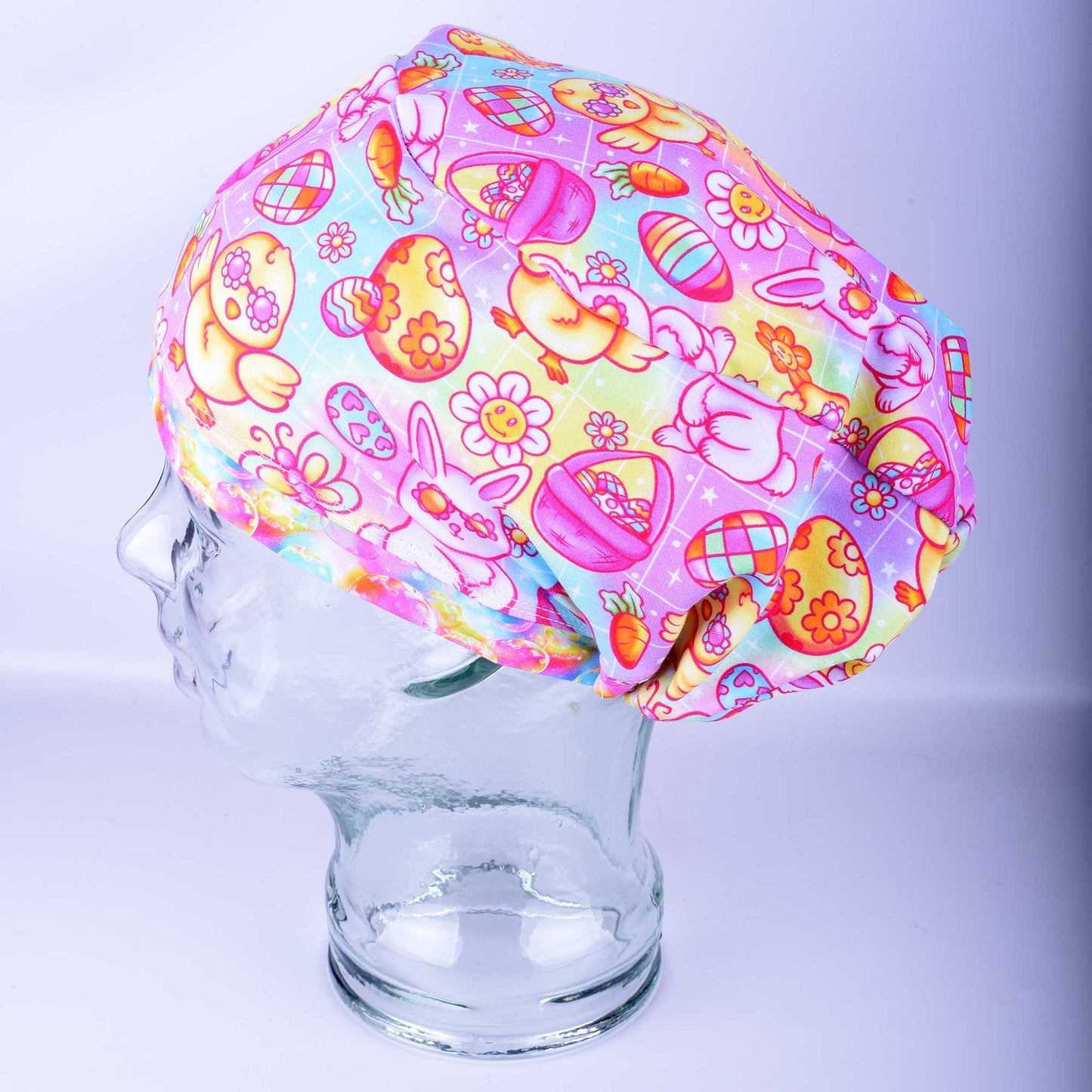 Handmade Euro-style scrub cap featuring a groovy Easter print with pastel bunnies, chicks, and eggs on a white background. Shown on a mannequin head to demonstrate full hair coverage and a sleek fit.