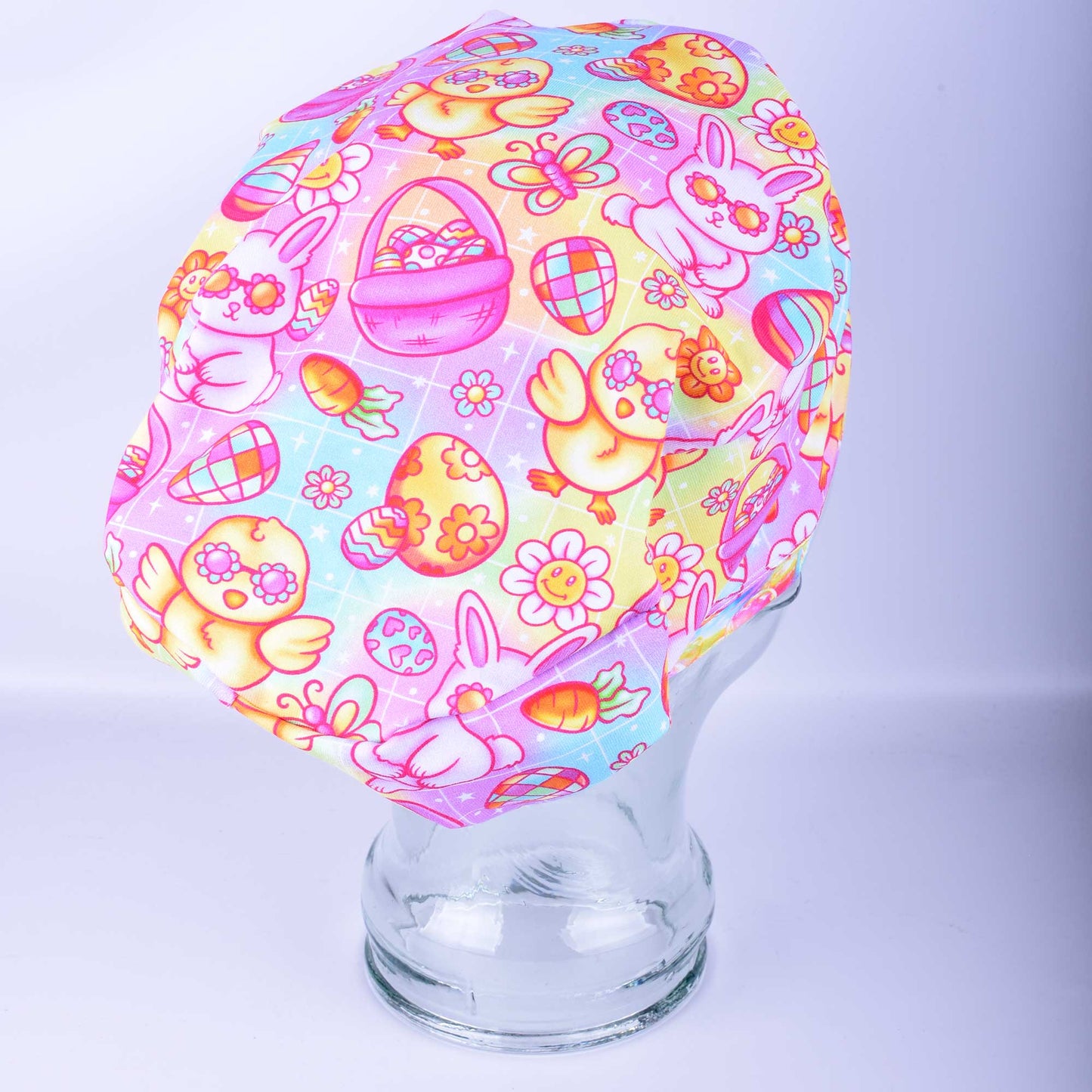 Side profile of a stretchy knit scrub cap in a pastel Easter bunny print, highlighting the toggle adjustment at the back and the secure fit around the ears.