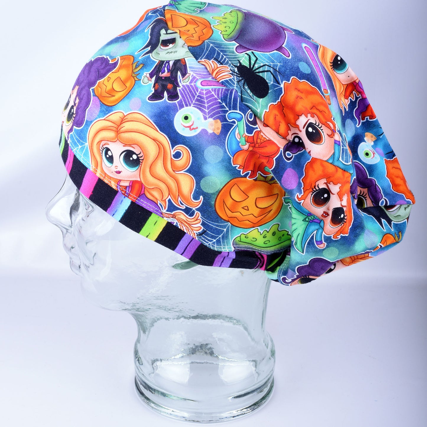 A colorful Halloween-themed scrub cap with cartoon characters and spooky motifs, displayed on a clear glass mannequin head against a light gray background.
