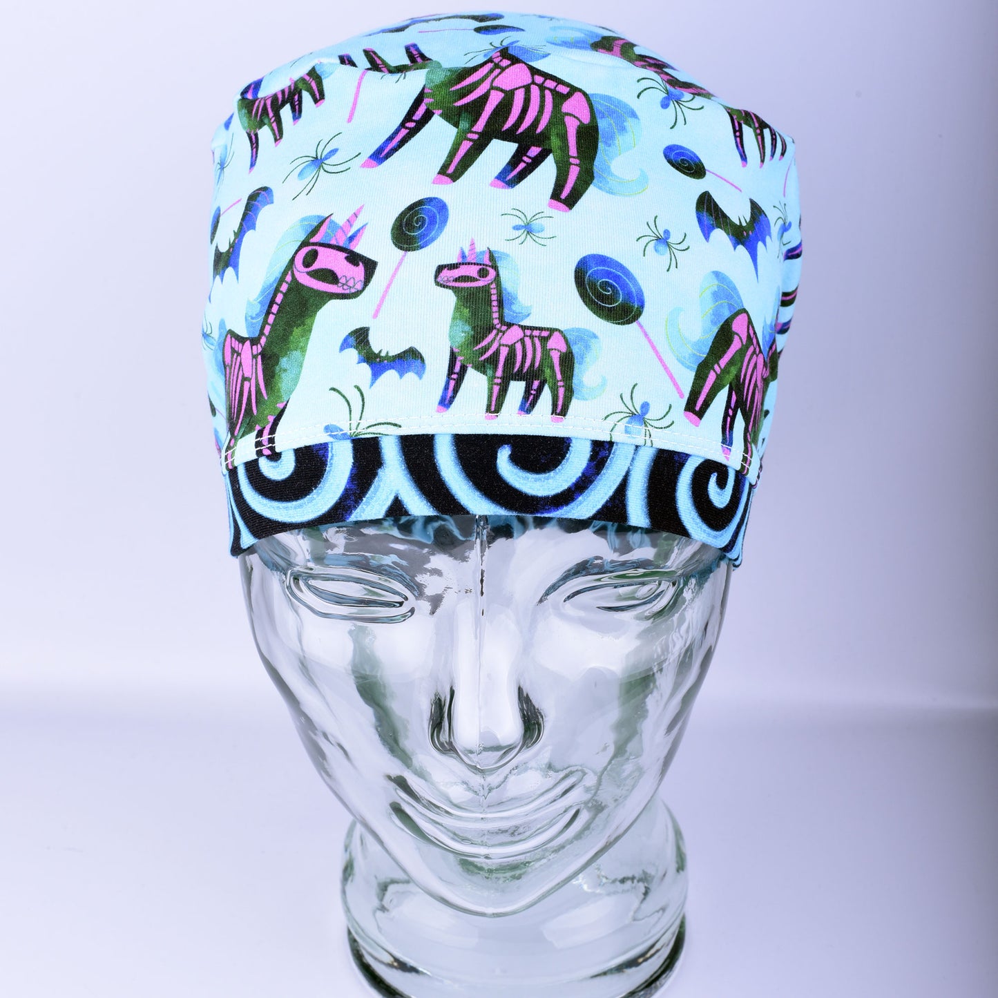 Front view of unicorn skeleton scrub cap on a clear mannequin head showing full coverage fit and light blue background pattern.
