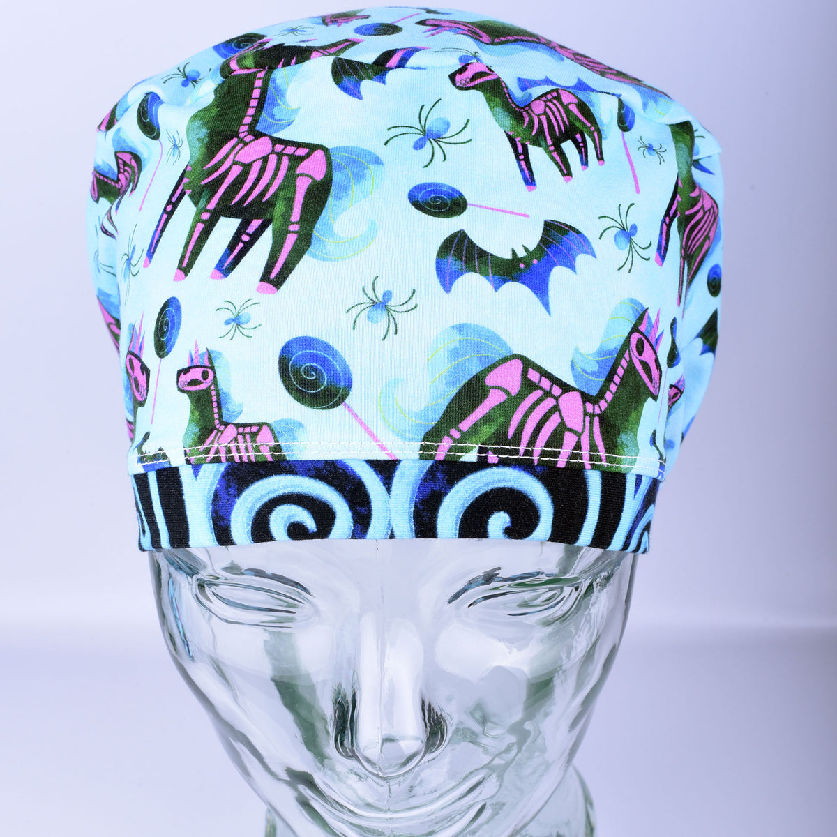 Front view of unicorn skeleton scrub cap on a clear mannequin head showing full coverage fit and light blue background pattern.