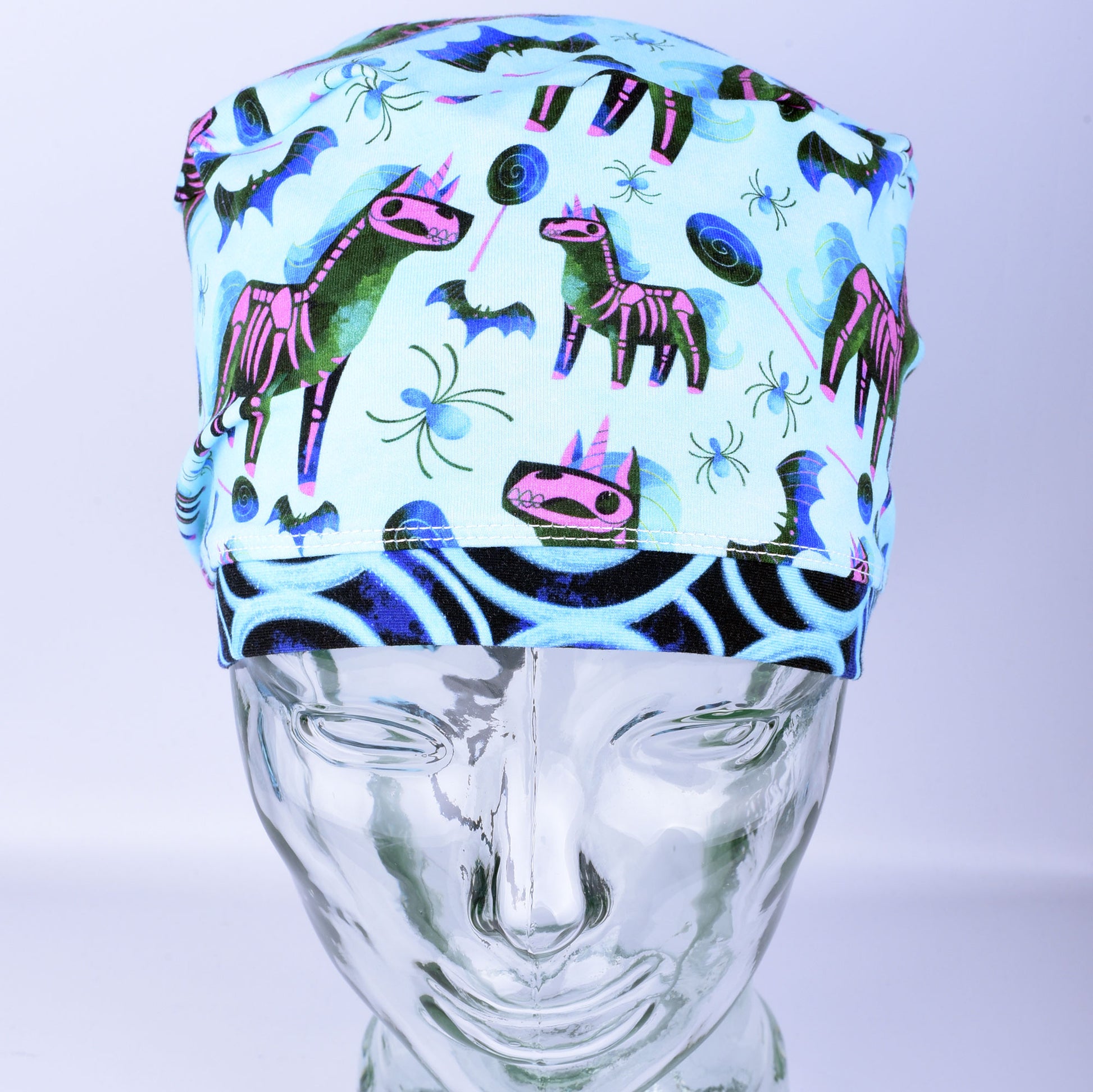 Front view of unicorn skeleton scrub cap on a clear mannequin head showing full coverage fit and light blue background pattern.