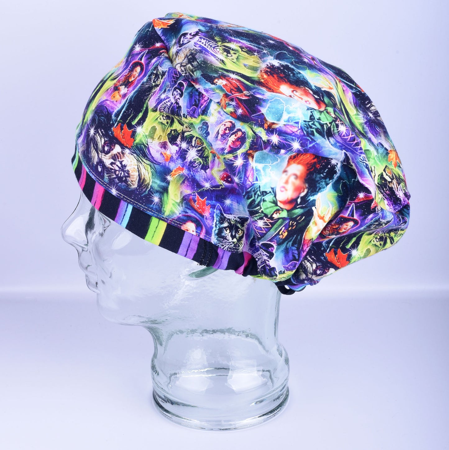 Halloween witches scrub cap in Euro-style full coverage on a clear mannequin head, featuring a vibrant colorful witch print with a purple-and-black striped rim.