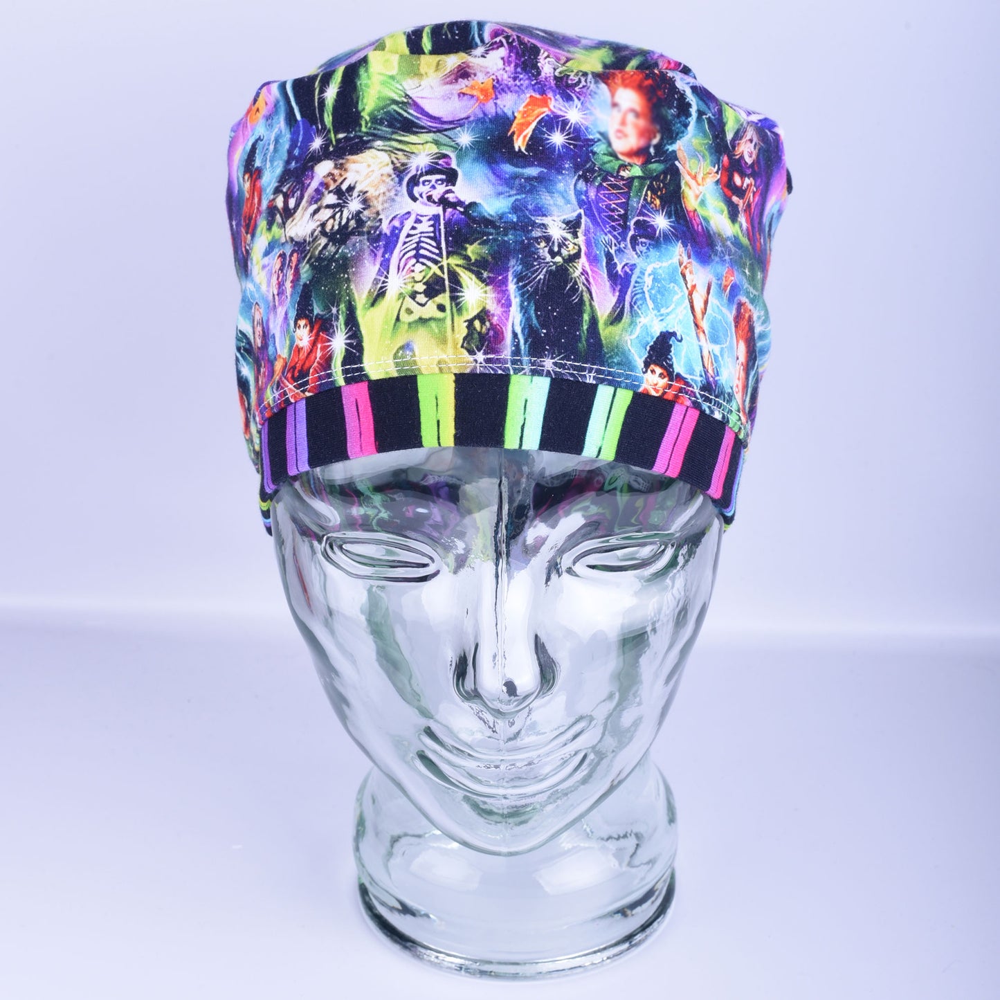 Front view of an adjustable Halloween witch pattern scrub cap with a purple striped trim band on a clear display head.