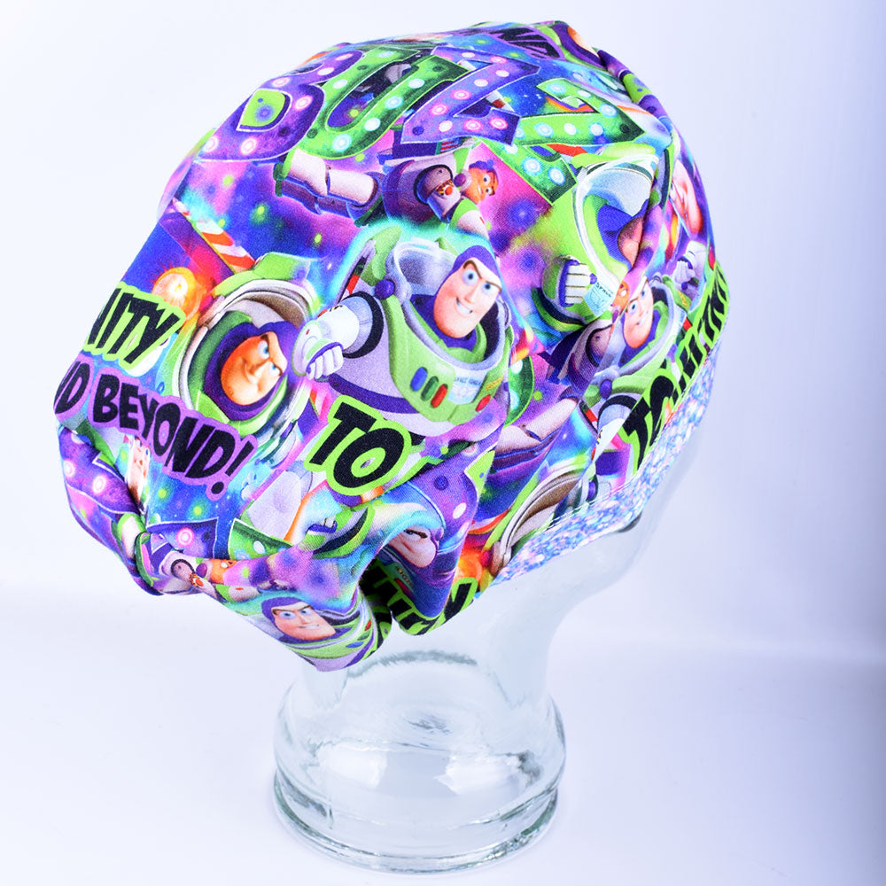 Side view of a full-coverage surgical scrub cap on a clear mannequin head, featuring a vibrant cartoon astronaut and outer space pattern on a crisp white background.