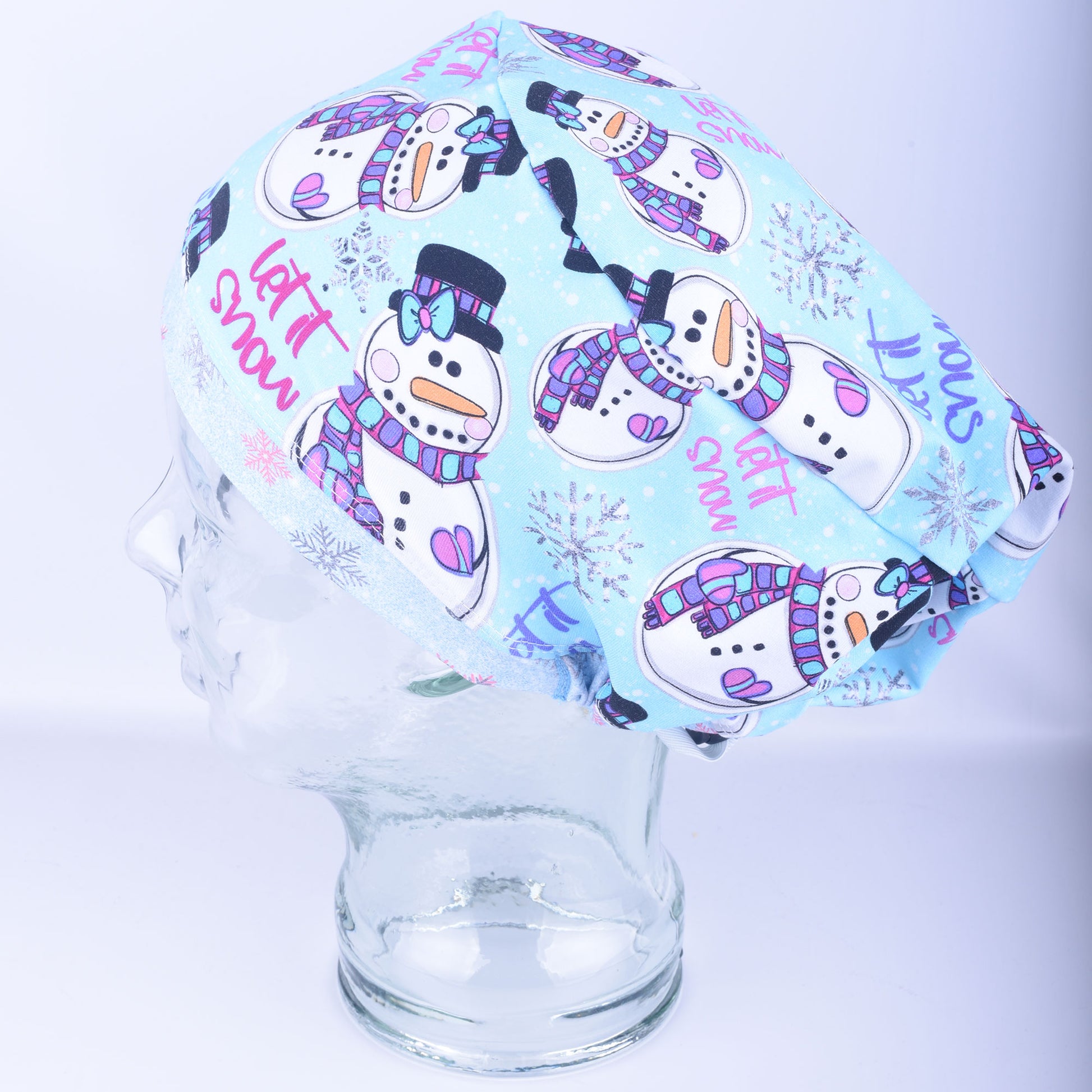 A light blue Euro-style scrub cap featuring a festive, colorful snowman and snowflake pattern, displayed on a clear mannequin head to showcase its full-coverage fit.