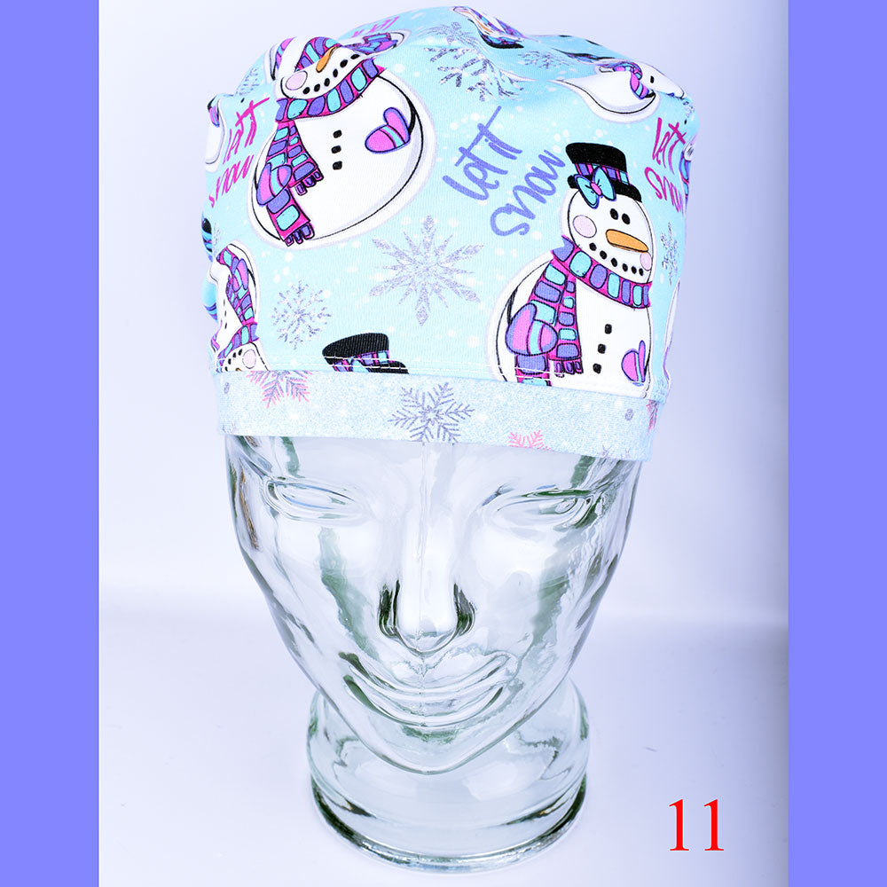 A light blue Euro-style scrub cap featuring a festive, colorful snowman and snowflake pattern, displayed on a clear mannequin head to showcase its full-coverage fit.
