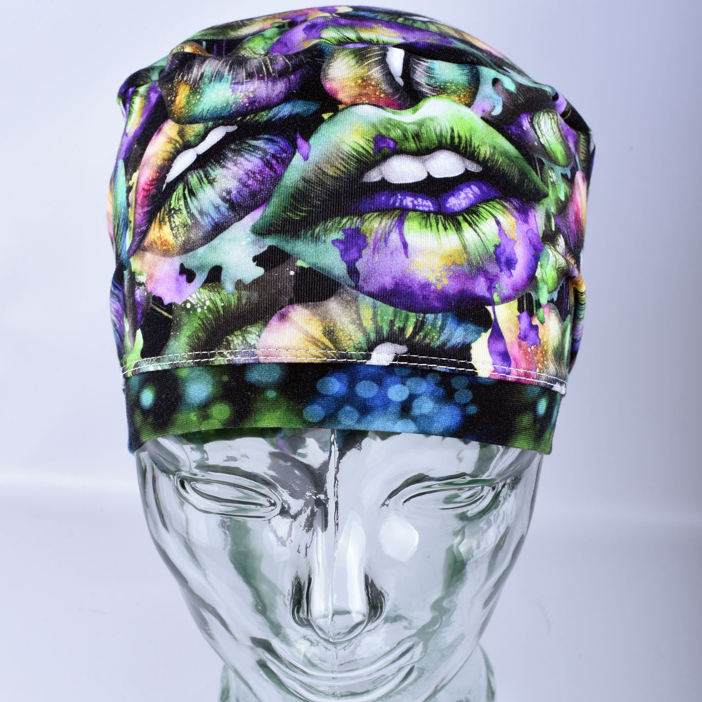 Full coverage Euro-style scrub cap featuring a festive Lucky Lips print with vibrant green, purple, and gold multicolor lips on a clean white background, displayed on a mannequin head to show a secure fit.