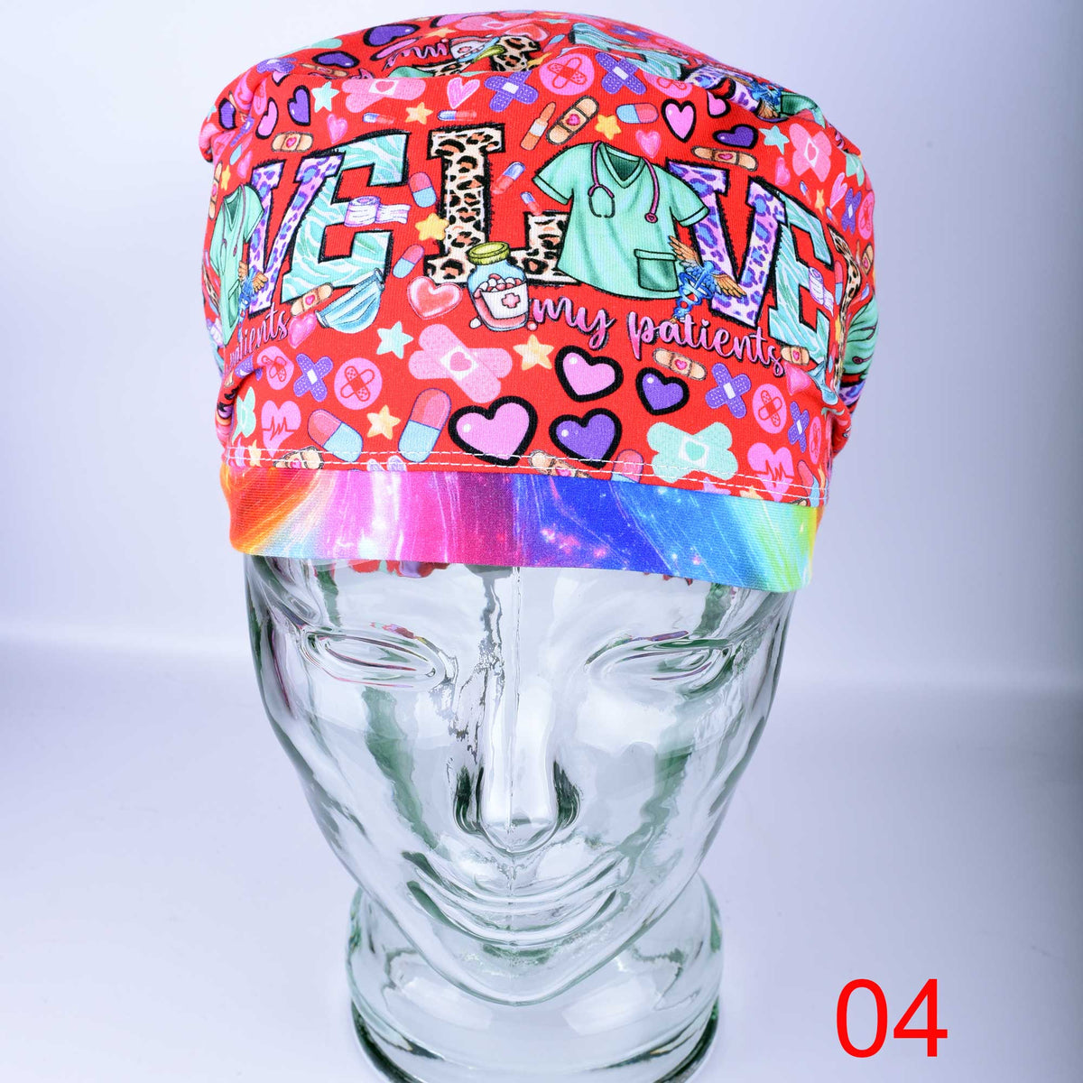 A colorful patterned surgical cap displayed on a clear mannequin head. The cap features a red background with a busy pattern of hearts, medical icons, and the word 'LOVE' in large letters, along with a rainbow gradient band at the bottom.