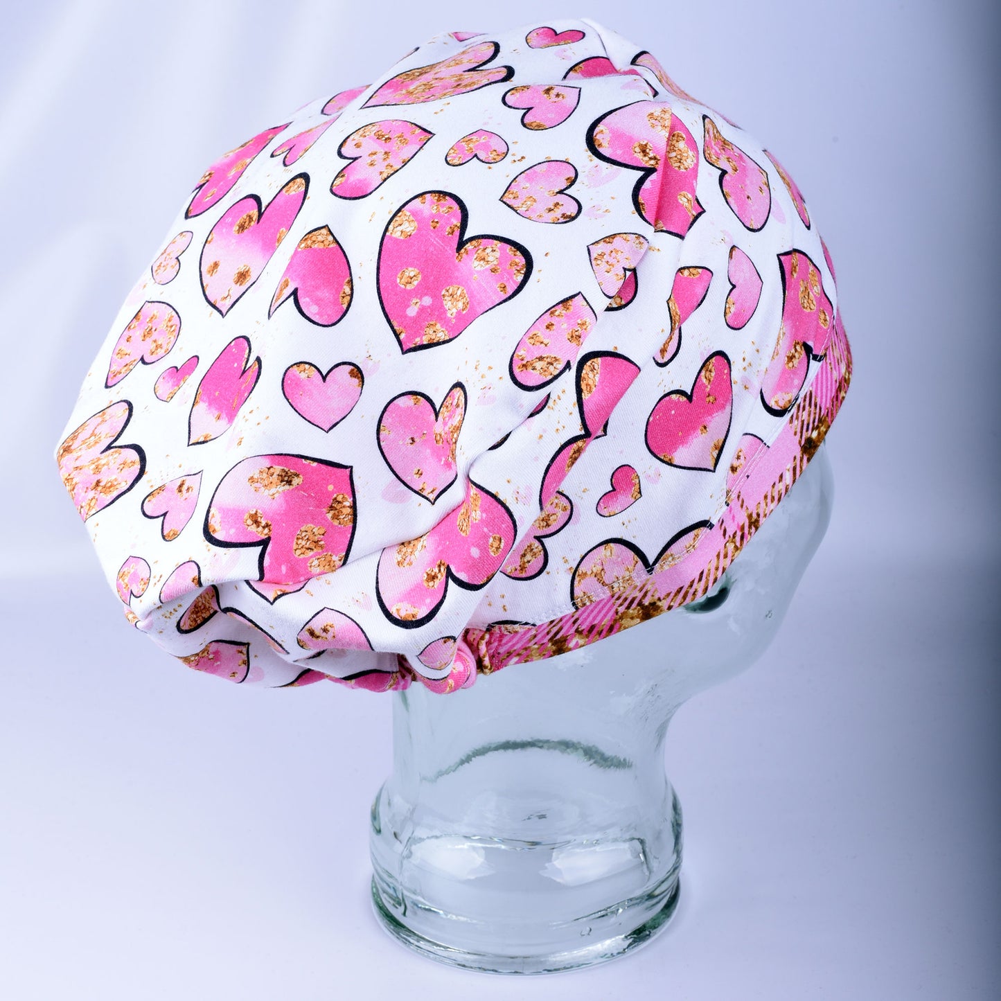 Side profile of a European style full coverage scrub cap in pink and gold heart print.