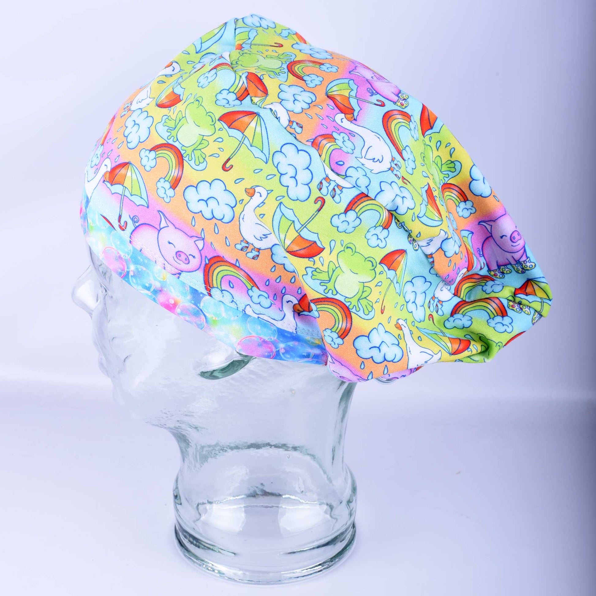 Euro-style full coverage scrub cap featuring a colorful raindrops and rainbows print on a blue background, shown on a mannequin head.
