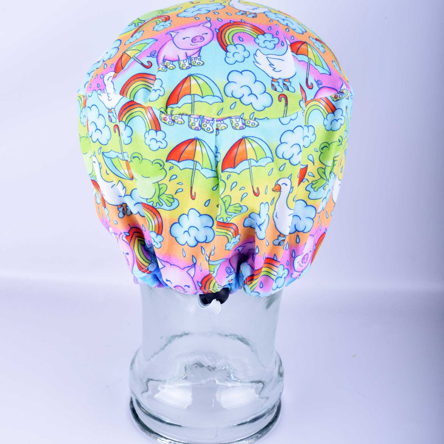 Euro-style full coverage scrub cap featuring a colorful raindrops and rainbows print on a blue background, shown on a mannequin head.
