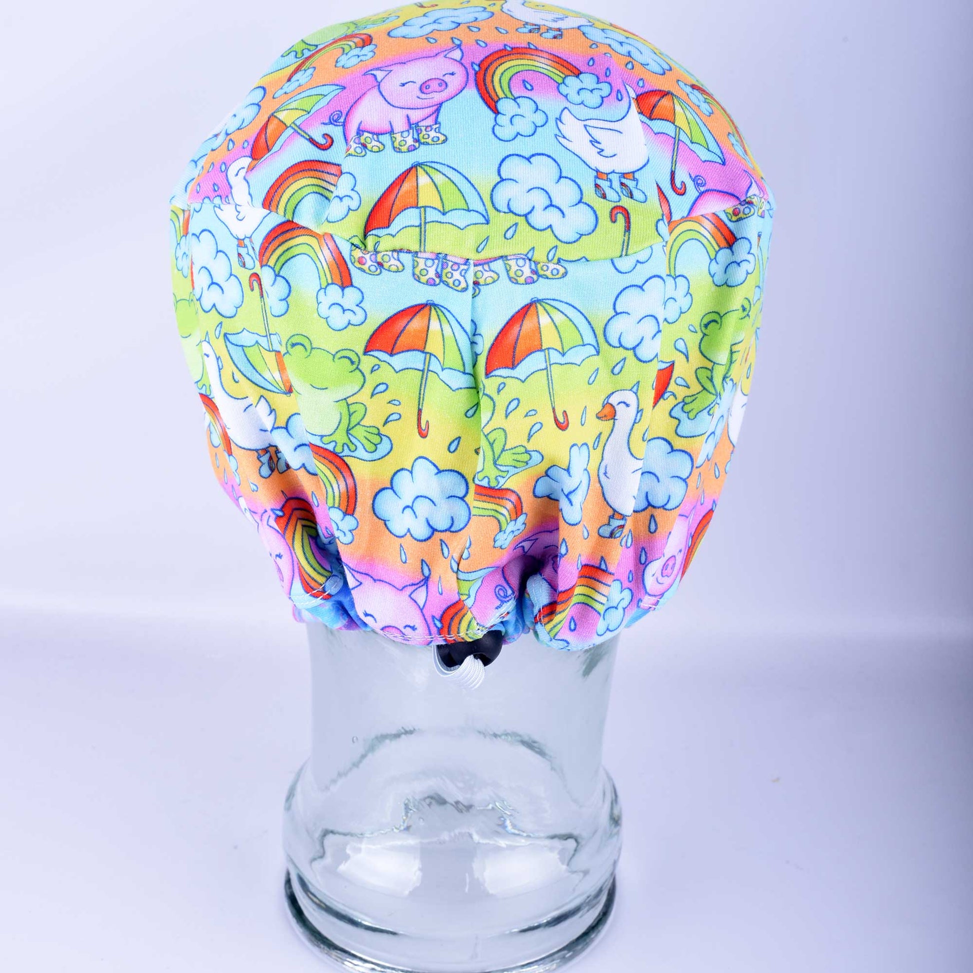 Euro-style full coverage scrub cap featuring a colorful raindrops and rainbows print on a blue background, shown on a mannequin head.