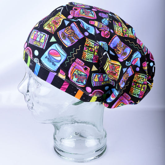 A multicolor retro-themed scrub cap featuring a vibrant pop-art pattern of candy, bubblegum, and soda cans on a black background, displayed on a clear glass mannequin head.