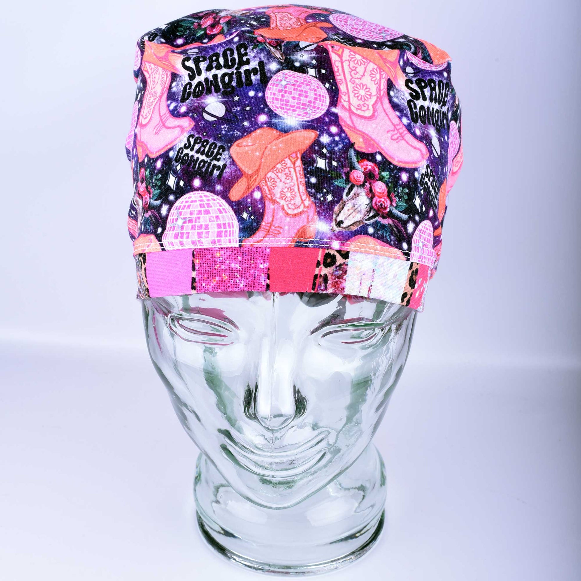 Close-up of the Space Cowgirl scrub cap fabric featuring a vibrant pattern of disco balls, cowboy boots, stars, and crescent moons on a dark background.