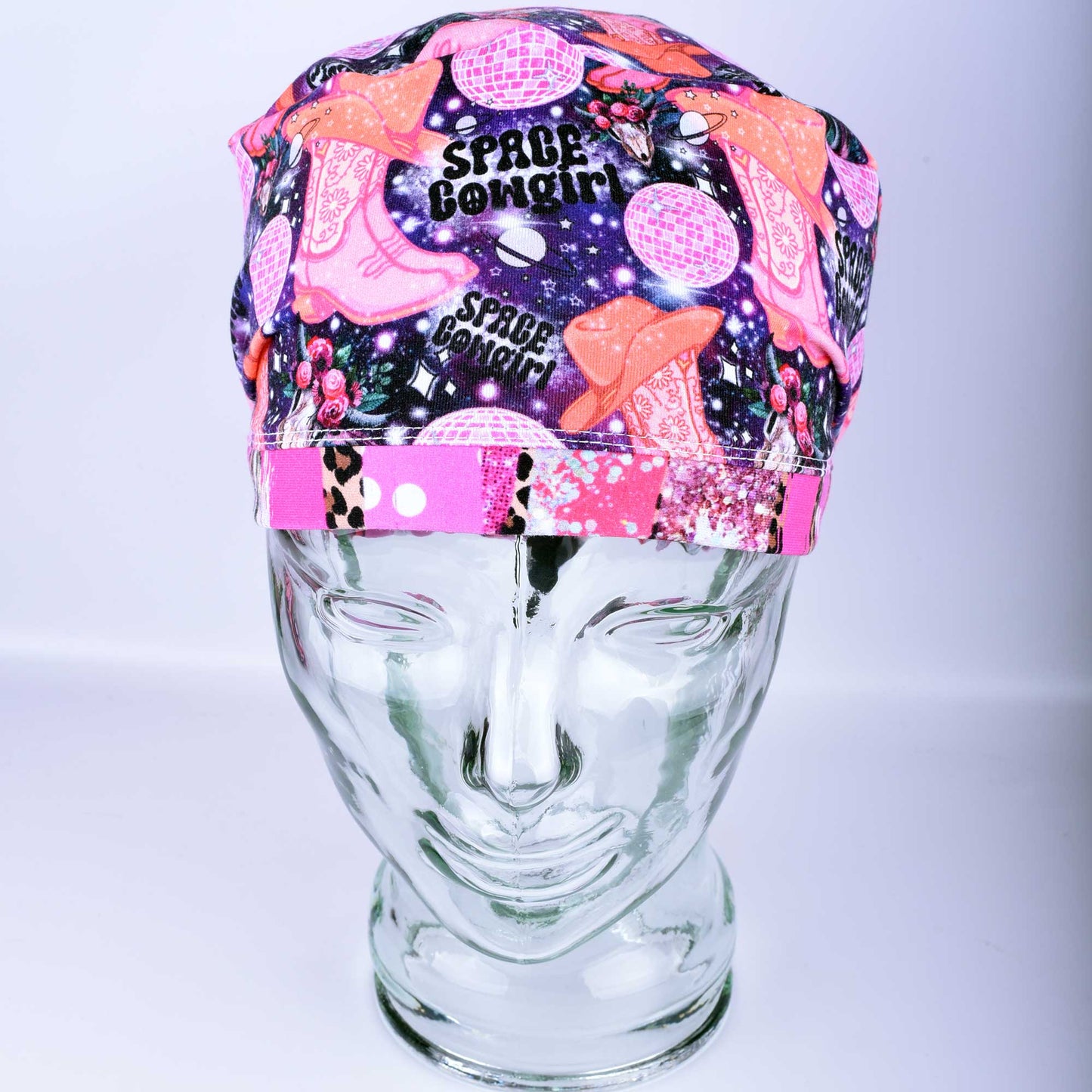 Close-up of the Space Cowgirl scrub cap fabric featuring a vibrant pattern of disco balls, cowboy boots, stars, and crescent moons on a dark background.