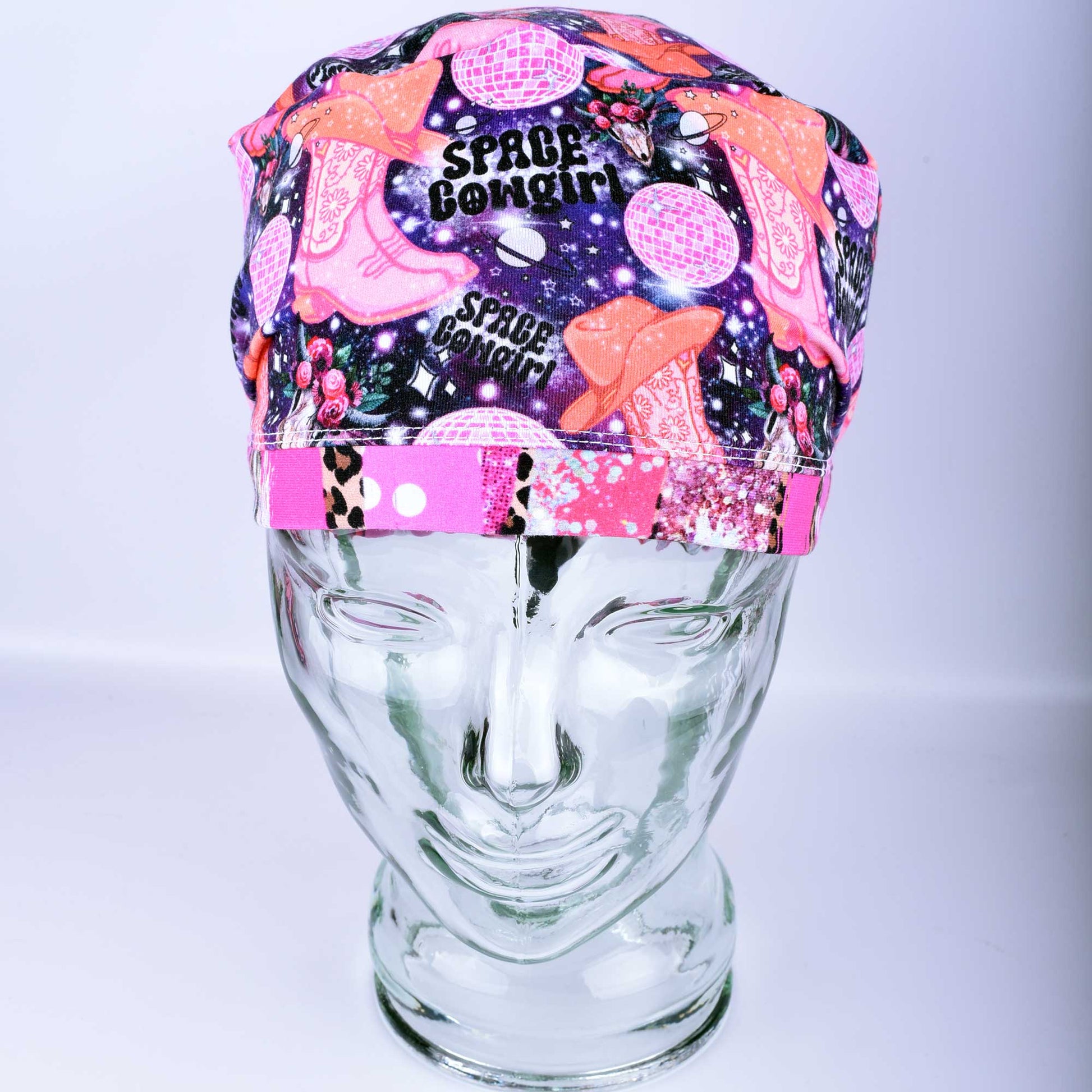 Close-up of the Space Cowgirl scrub cap fabric featuring a vibrant pattern of disco balls, cowboy boots, stars, and crescent moons on a dark background.